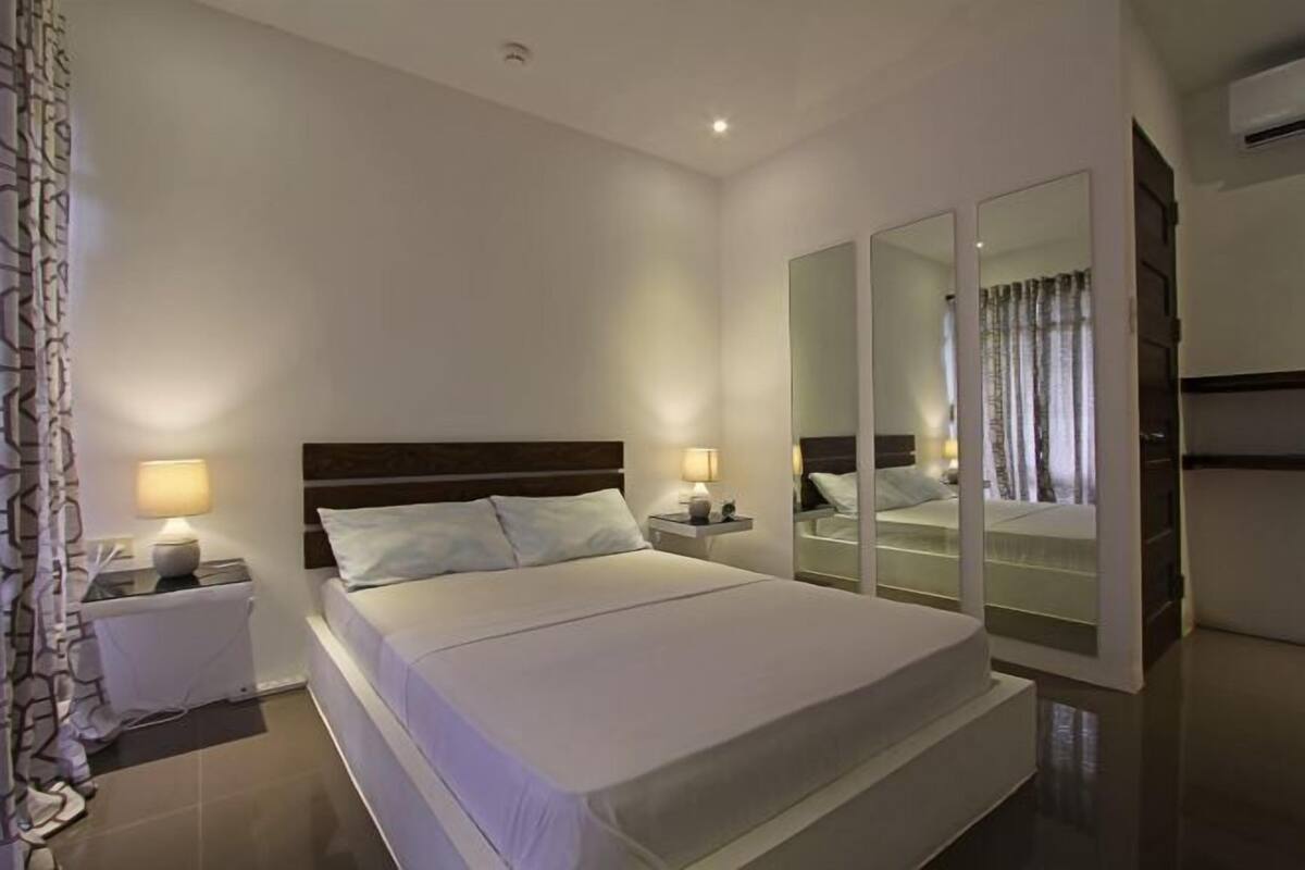 A modern hotel room with a large bed, bedside lamps, a mirror, and a wardrobe.
