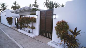 Stylish building with a minimalist design, featuring a white exterior and a dark gate, surrounded by palm trees.