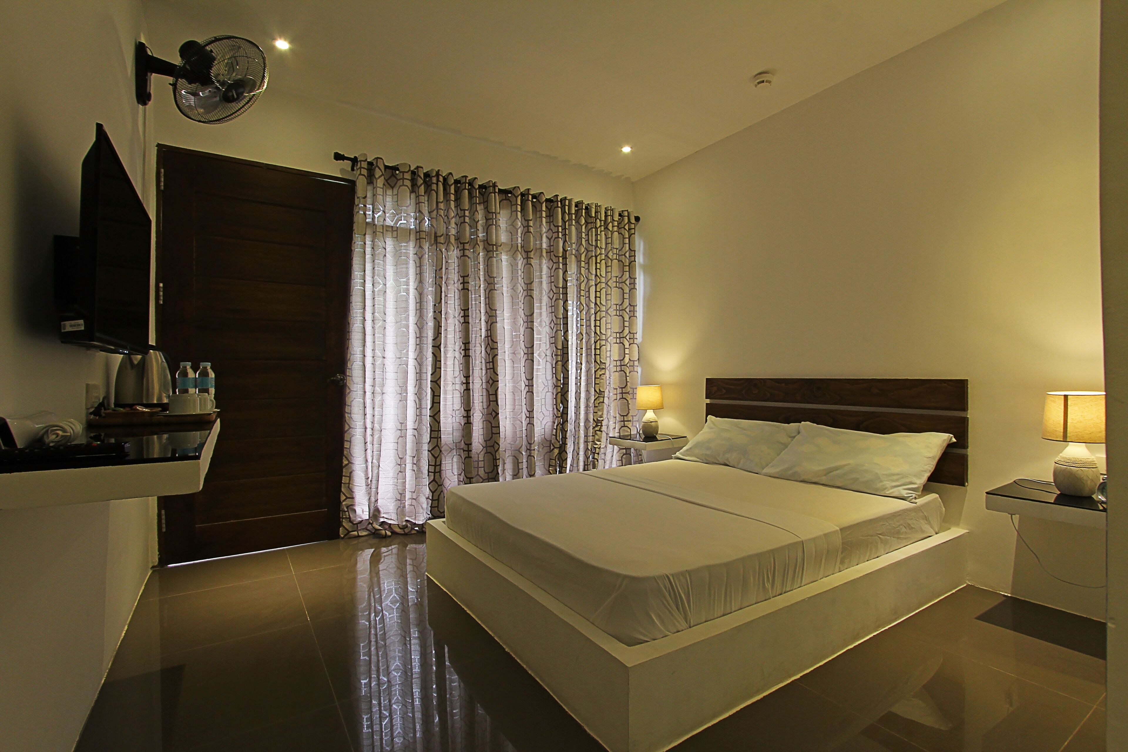 A modern hotel room with a large bed, bedside tables with lamps, a TV, and a wooden wardrobe.