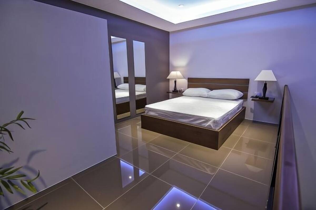 A modern hotel room with a large bed, bedside lamps, a mirror, and a plant.