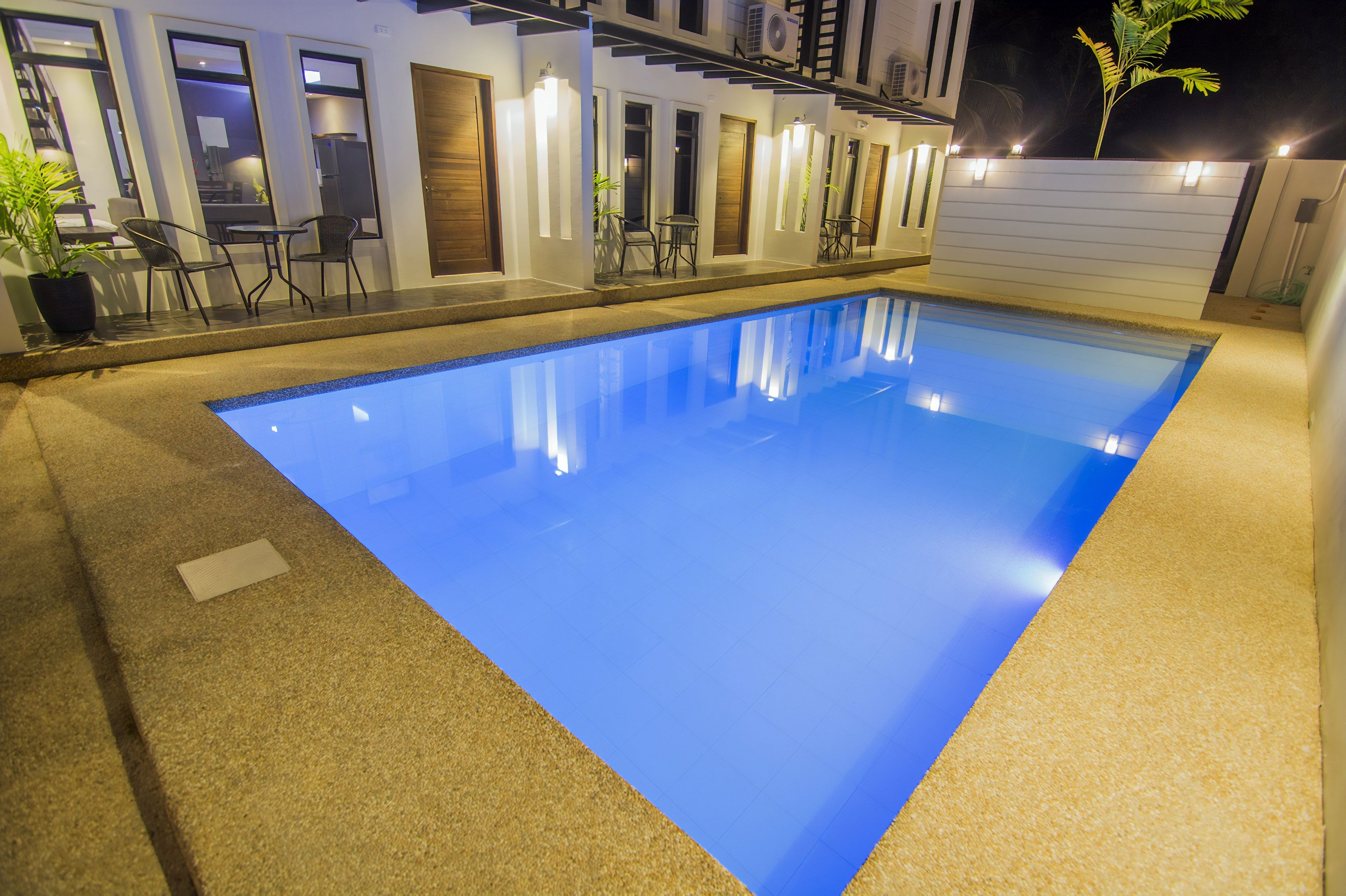 Ein Swimmingpool mit blauer Innenausstattung, umgeben von einer überdachten Terrasse mit Stühlen und Tischen.