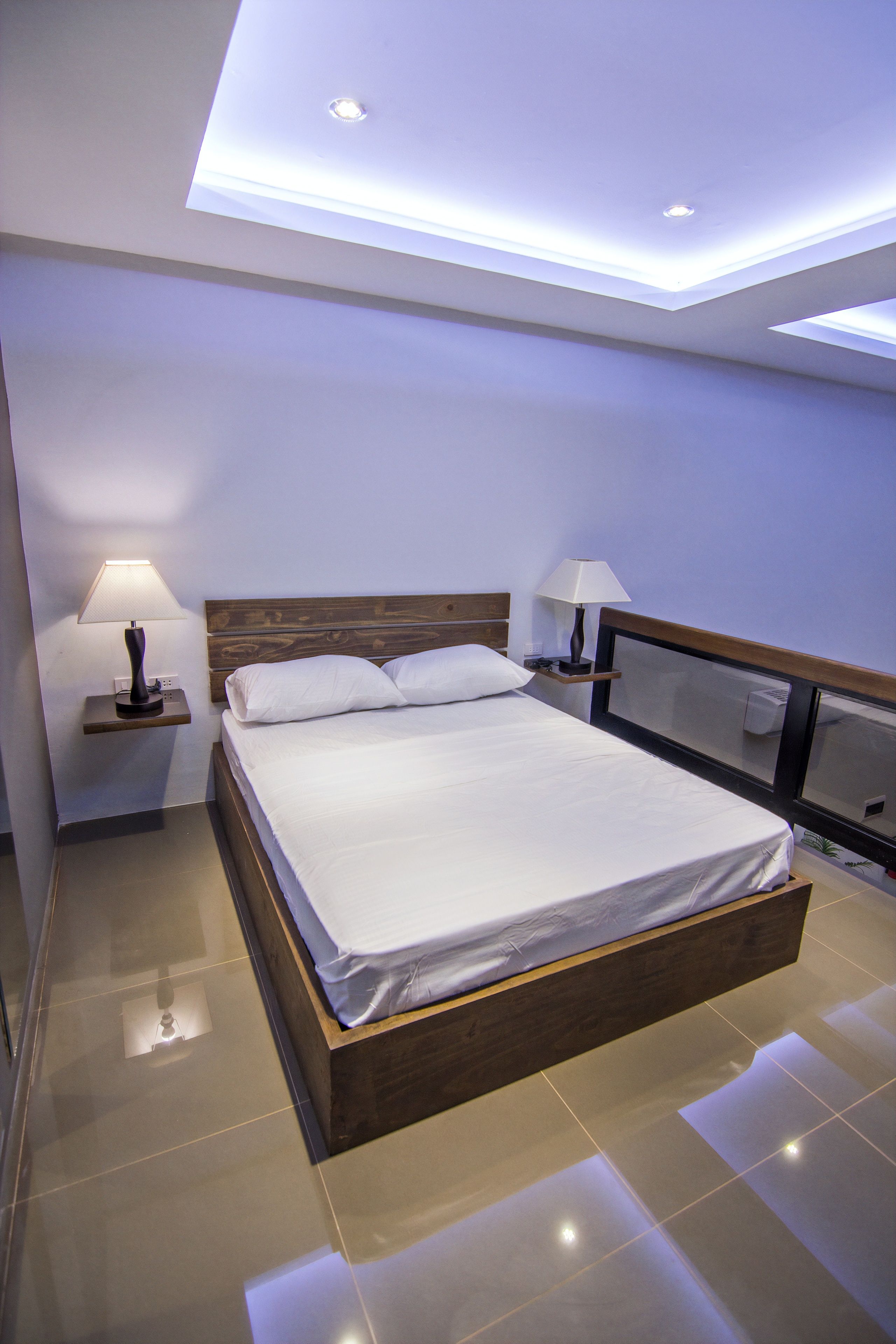 A modern hotel room with a large bed, two bedside tables with lamps, a wooden headboard, and a ceiling with recessed lighting.