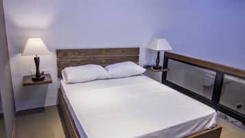 Una habitación de hotel moderna con una cama grande, dos mesitas de noche con lámparas, un cabecero de madera e iluminación empotrada en el techo.