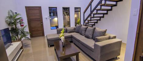 A modern living room with a sectional sofa, a coffee table, a TV, and a staircase.
