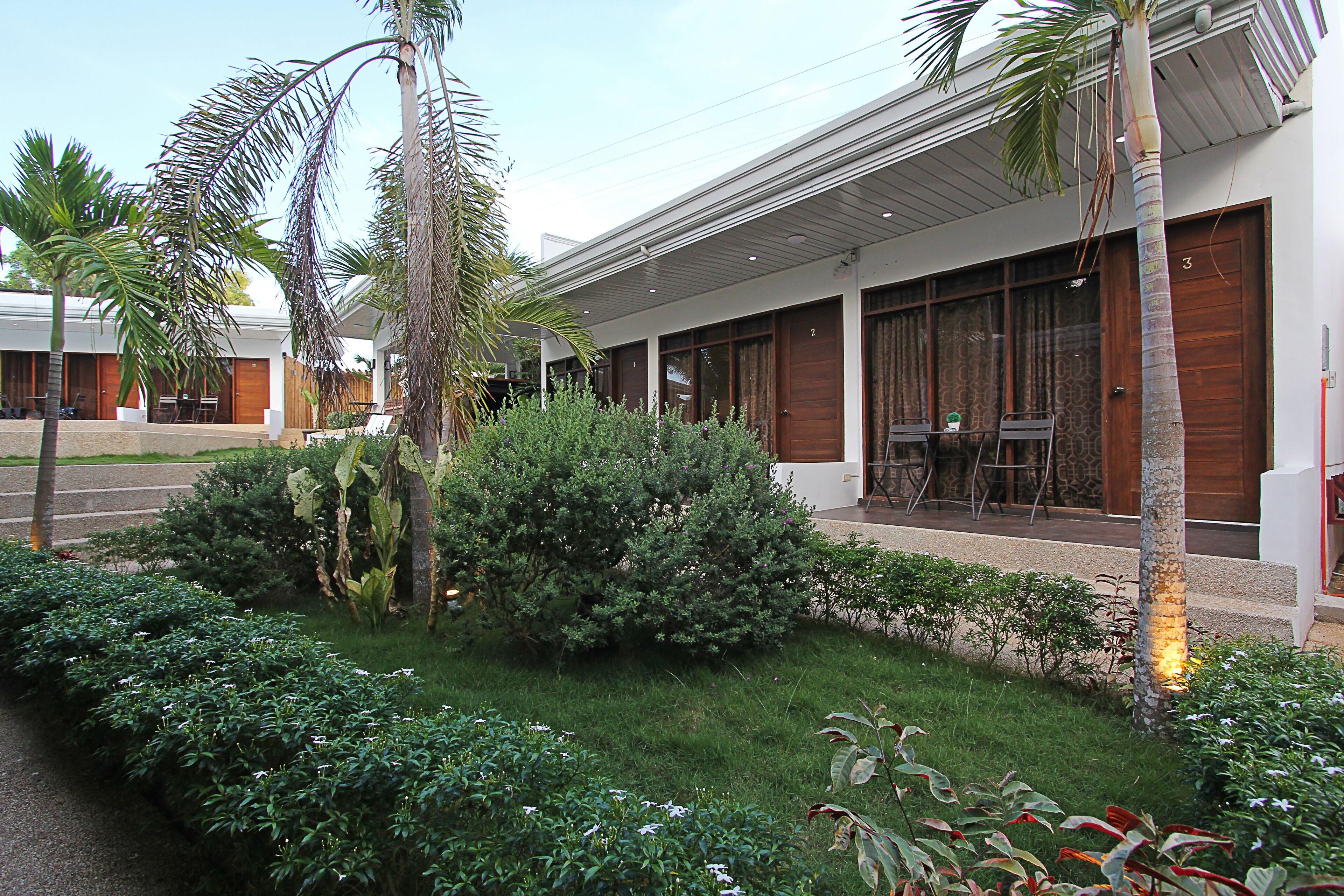 A modern hotel with a covered outdoor seating area, palm trees, and well-maintained gardens.