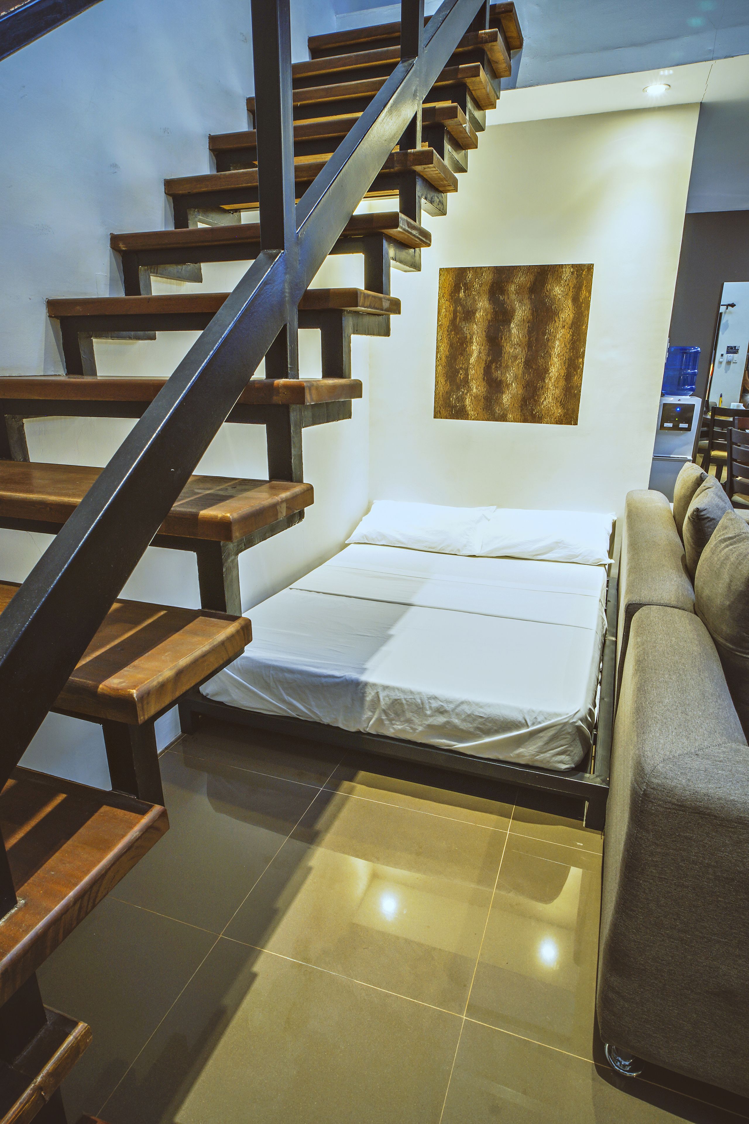 Un dormitorio con cama, sofá, escalera y un cuadro colgado en la pared.