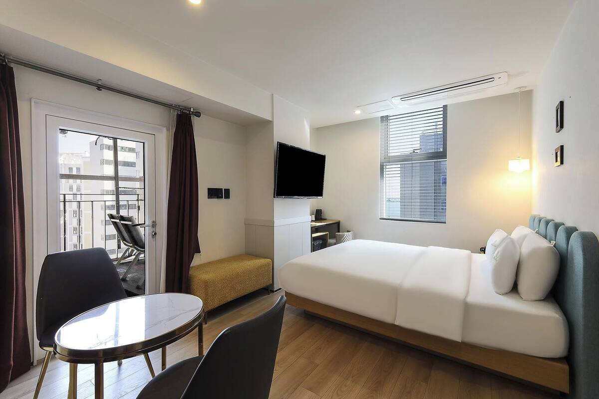 A modern hotel room with a bed, a desk, a chair, a TV, and a window.