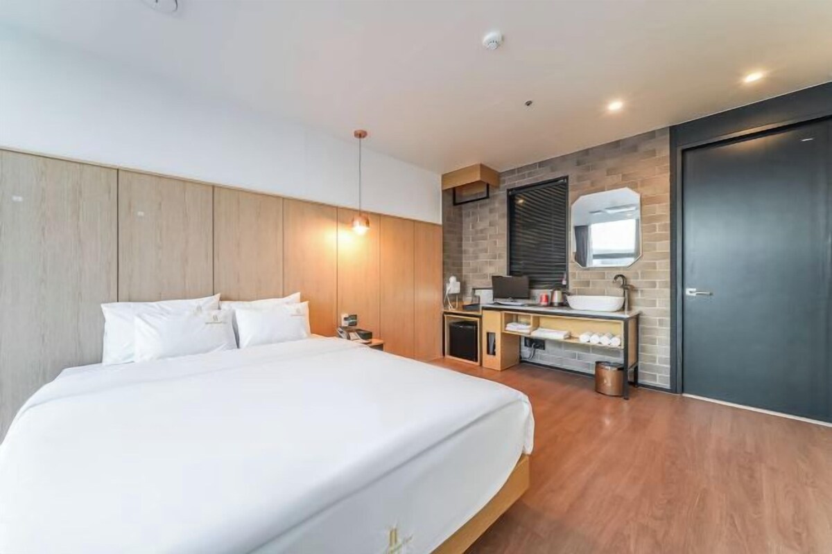 A modern hotel room with a large bed, a desk with a sink, and a mirror.