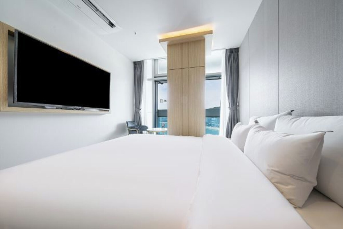 Una habitación de hotel moderna con una cama grande, un televisor de pantalla plana en la pared y vistas de la ciudad a través de amplios ventanales.