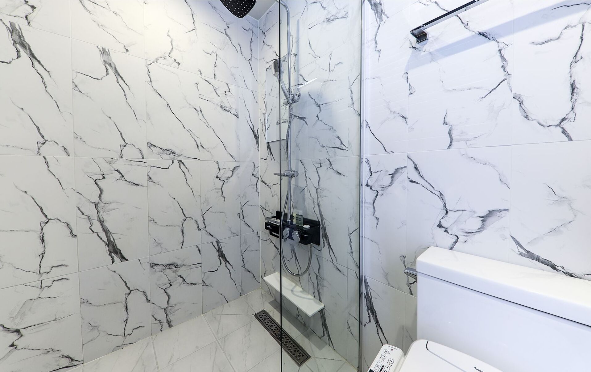 A modern bathroom with a glass-enclosed shower, marble walls, and a white toilet.