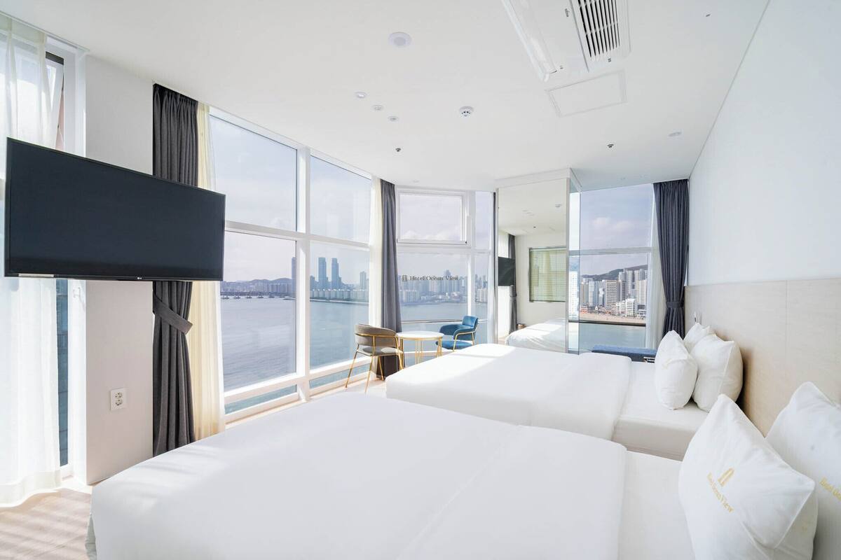 A hotel room with two beds, a TV, a city view, and a small table with chairs.