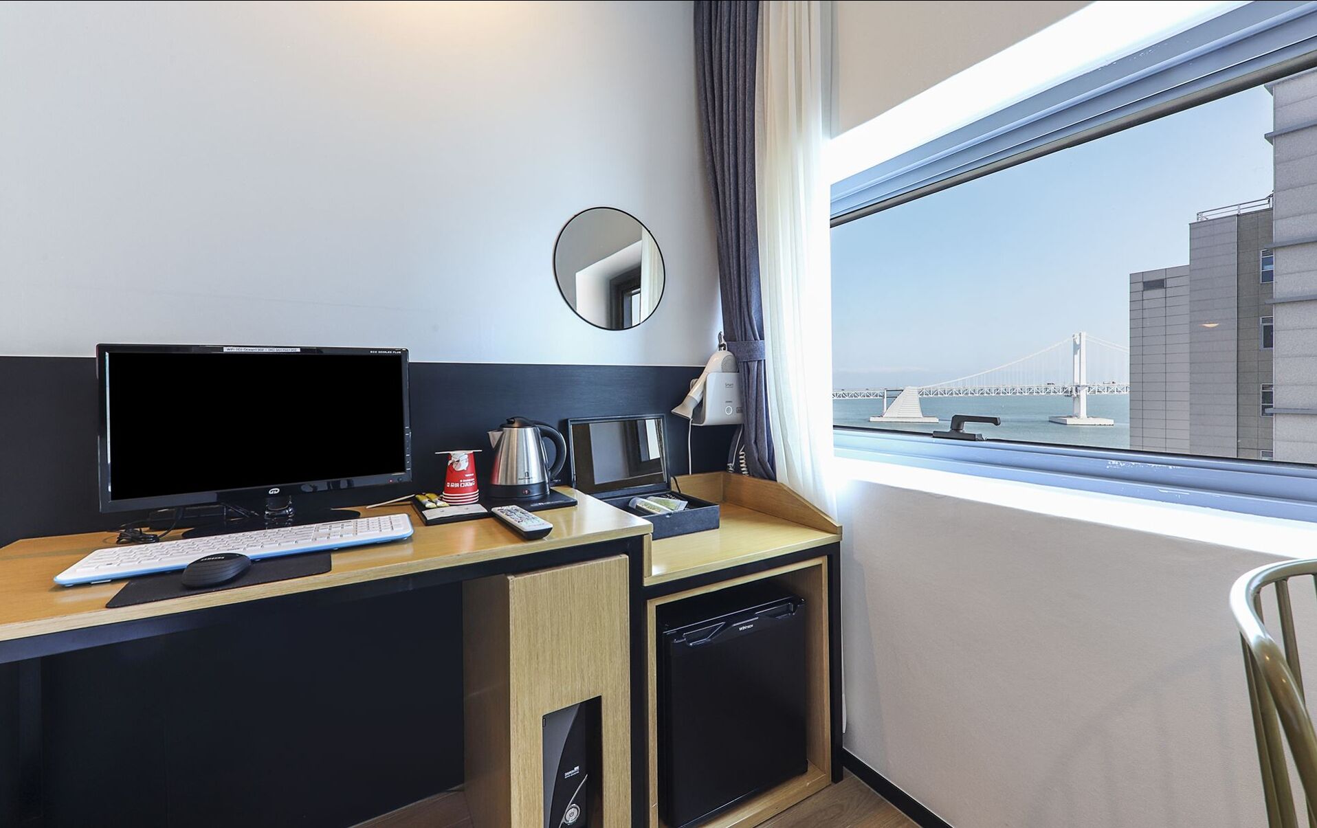 Une chambre d’hôtel équipée d’un bureau, d’un ordinateur, d’un clavier et offrant une vue sur un pont.