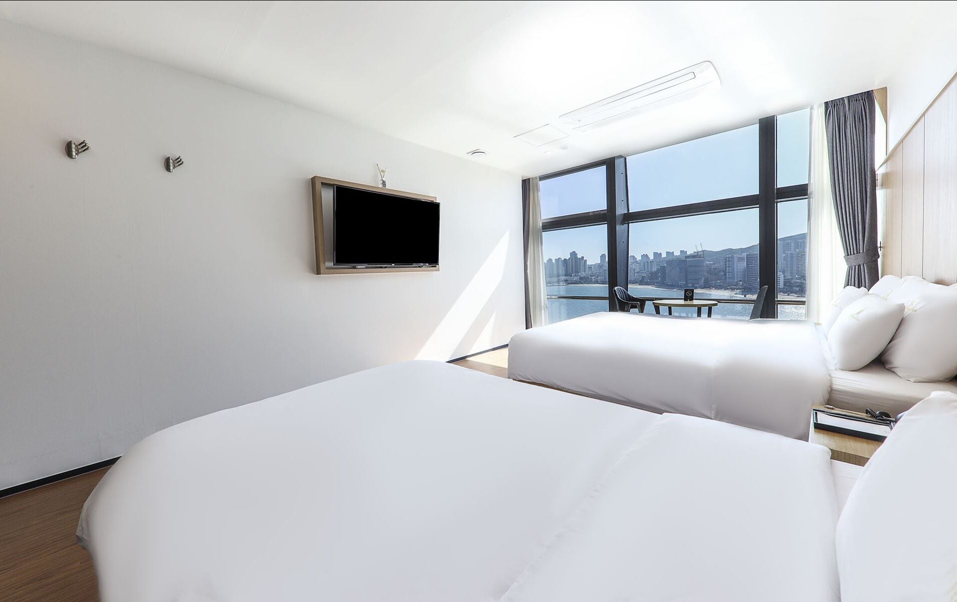 Une chambre d’hôtel moderne avec deux lits, un téléviseur à écran plat, une grande fenêtre donnant sur la ville et une petite table.