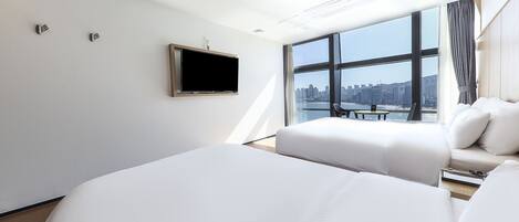 Une chambre d’hôtel moderne avec deux lits, un téléviseur à écran plat, une grande fenêtre donnant sur la ville et une petite table.