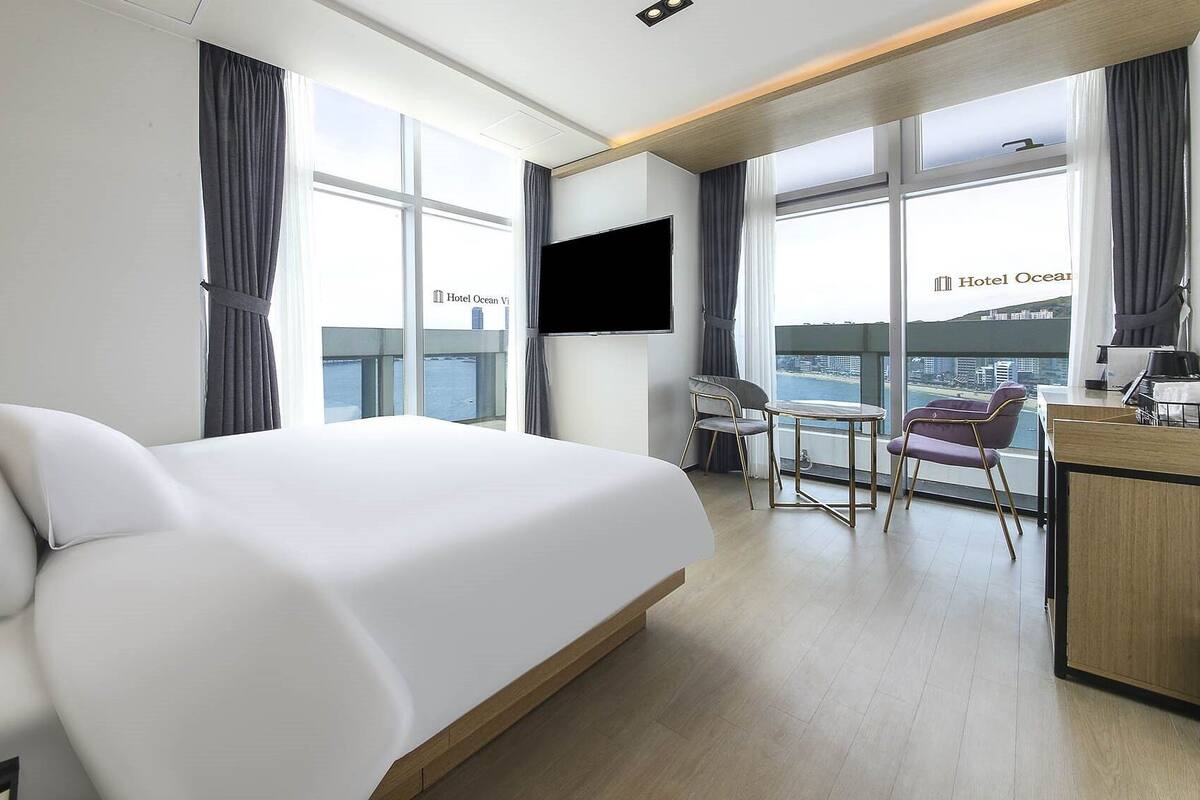 A modern hotel room with a large bed, a desk, and a view of the ocean.
