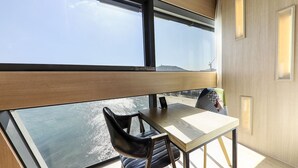 A modern room with a large window, a wooden table, a black chair, and a view of the sea.