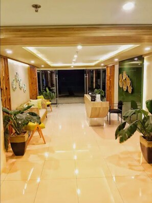 Un moderno vestíbulo de hotel con mostrador de recepción, zona de estar y plantas en macetas.