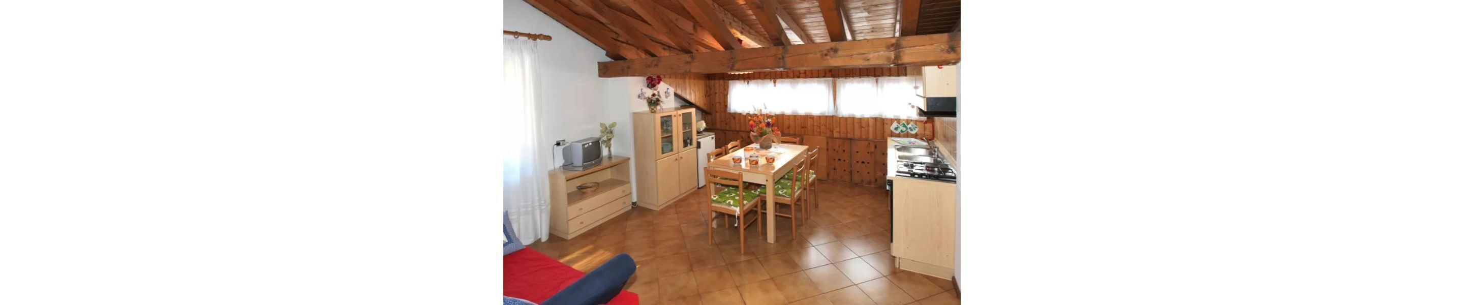 A compact kitchen with wooden cabinets, a dining table with chairs, and a small refrigerator.