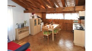 A compact kitchen with wooden cabinets, a dining table with chairs, and a small refrigerator. - Casa Quercia (Falcade)