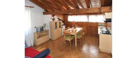 A compact kitchen with wooden cabinets, a dining table with chairs, and a small refrigerator.
