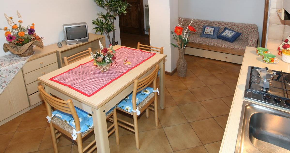 A compact kitchen with a dining table, chairs, a small TV, and a sofa in the background.