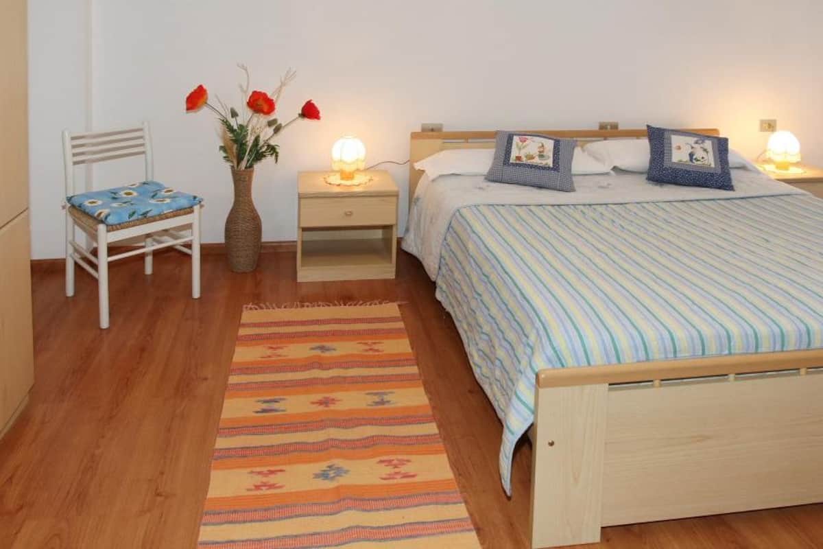 Une chambre à coucher avec un lit en bois, une table de chevet avec une lampe, une chaise et un vase rempli de fleurs.