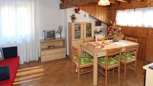 A cozy room with a wooden ceiling, a dining table with chairs, a television, and a cabinet with glass doors. - Casa Quercia (Falcade)
