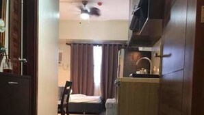 Habitación de hotel con cama, escritorio, silla, armario y ventilador de techo.