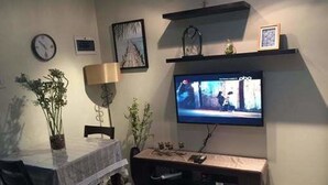 Una sala de estar con televisor sobre un mueble bajo, una mesa de comedor con sillas y una lámpara.