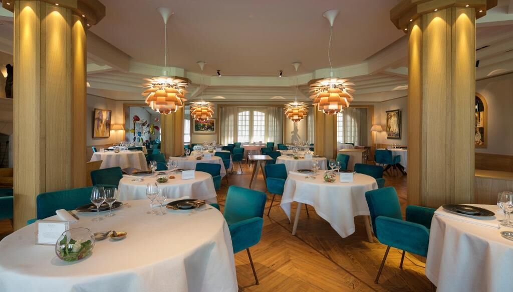 A restaurant with round tables, teal chairs, and large columns.