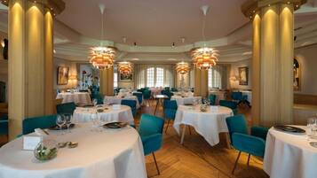 A restaurant with round tables, teal chairs, and large columns.