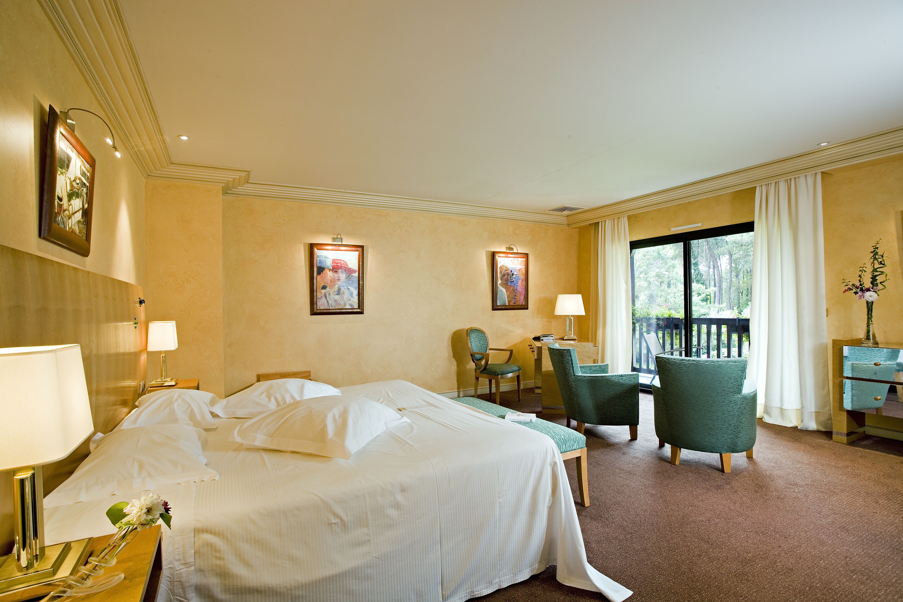Une chambre d’hôtel avec un grand lit, deux chaises, un bureau et un balcon avec des rideaux.
