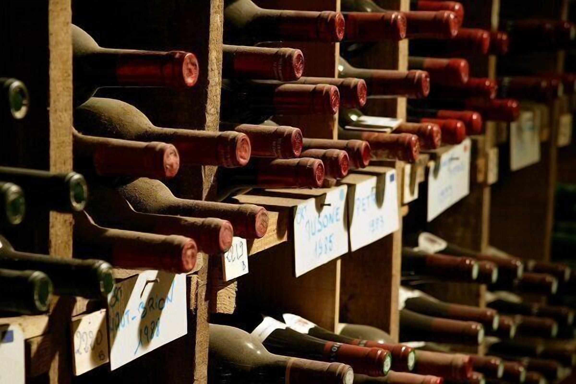 Une cave à vin avec des rangées de bouteilles de vin disposées sur des étagères en bois, chacune portant une étiquette indiquant l’année et le millésime.
