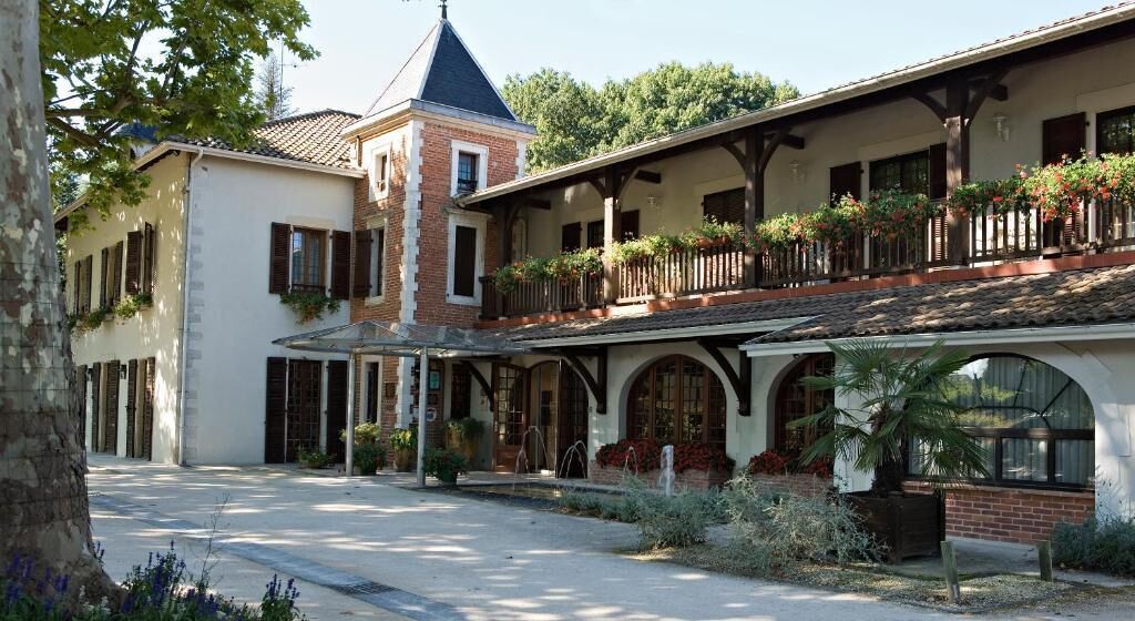 A traditional European-style building with a courtyard, arched windows, and a balcony with plants.