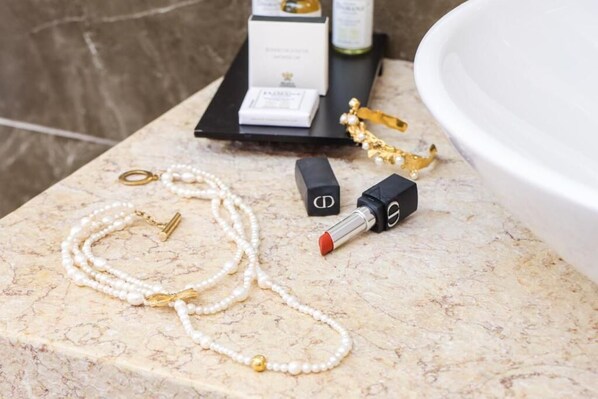 A marble countertop with a pearl necklace, gold jewelry, and a lipstick.