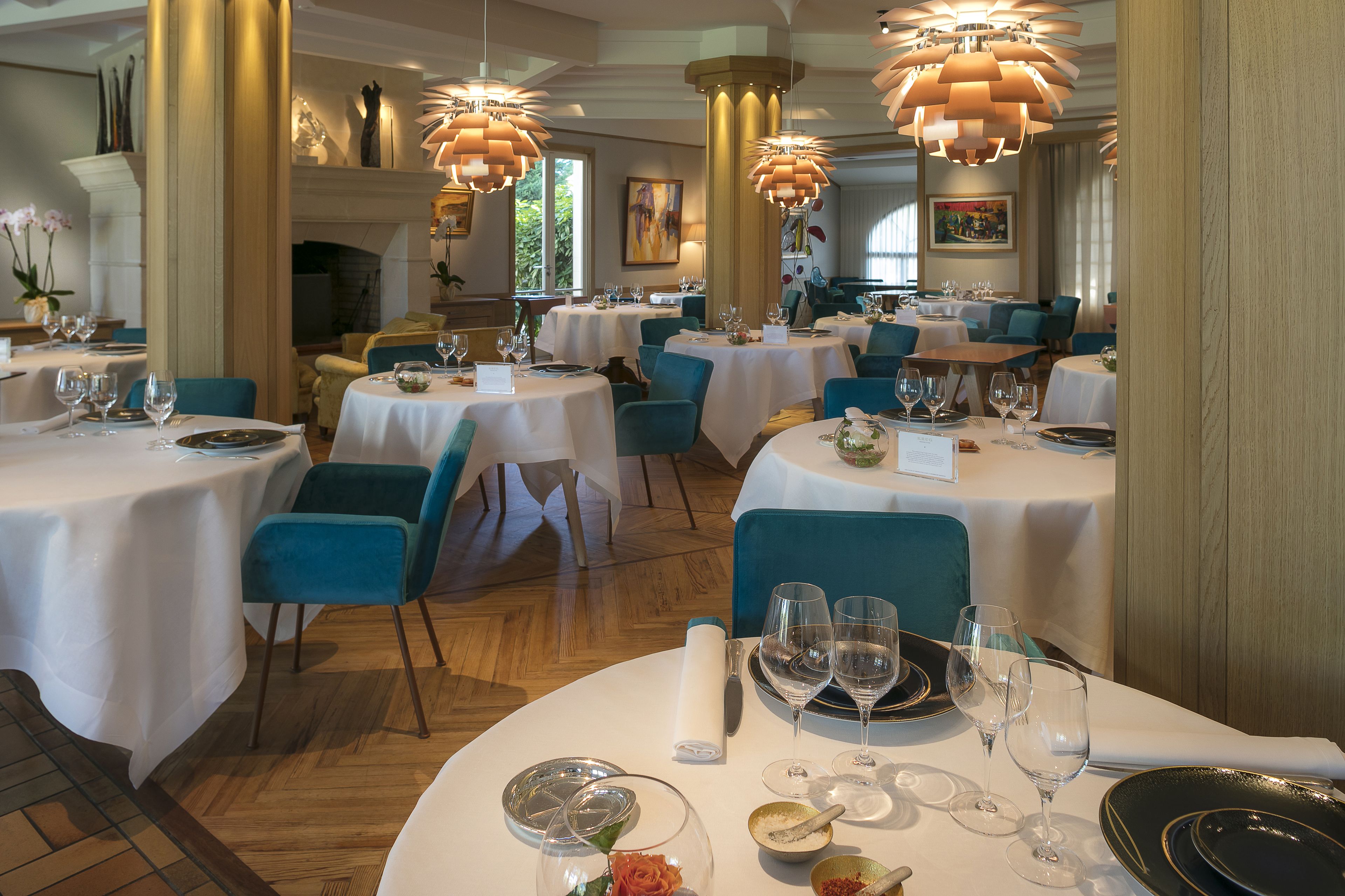 A restaurant with round tables, teal chairs, and gold accents.