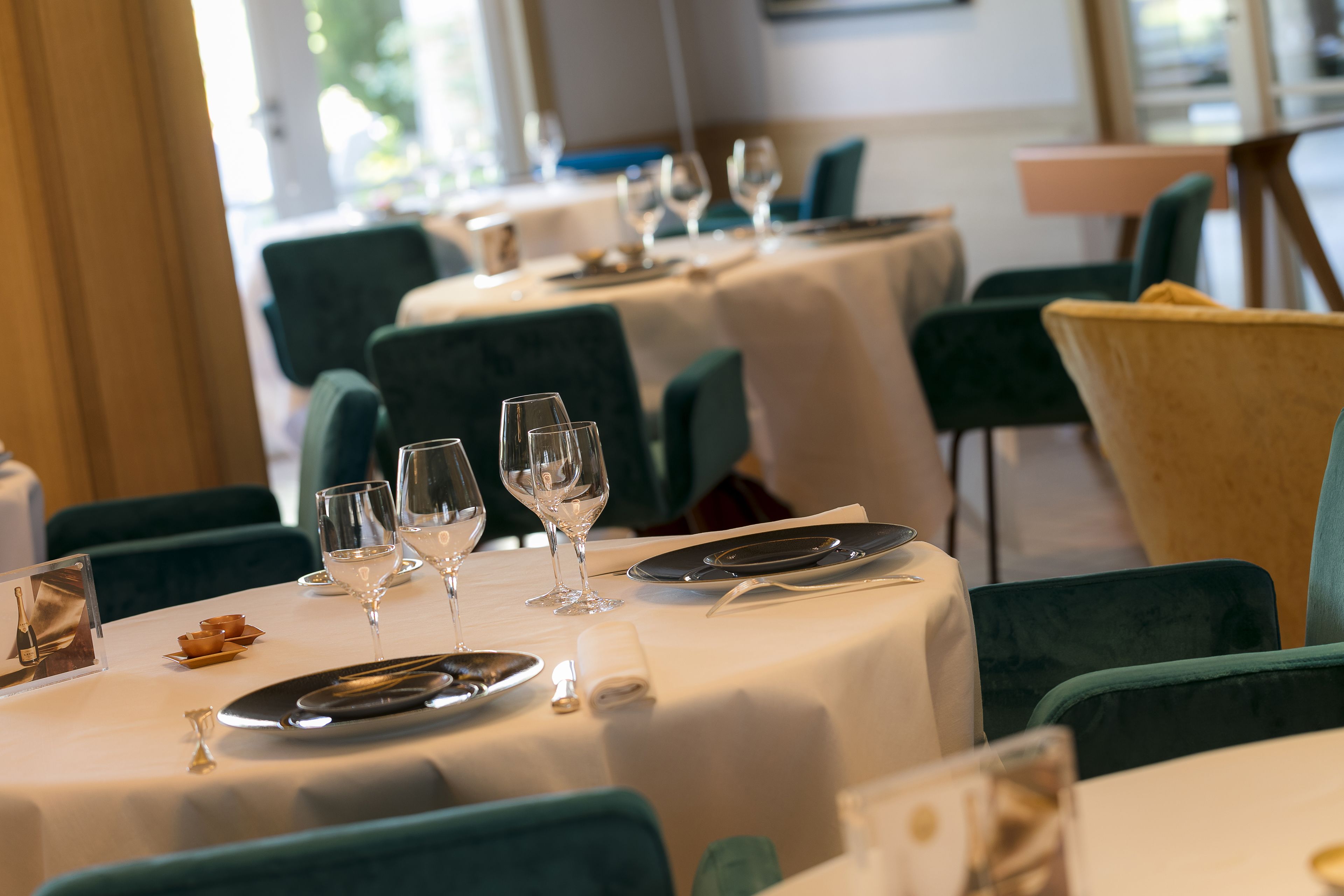 A restaurant with round tables set for dining, each with a white tablecloth, silverware, and wine glasses.
