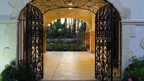 An ornate wrought iron gate leading to a courtyard with a tiled floor and a variety of plants. - LE RELAIS DE LA POSTE (Magescq)