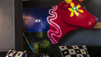A room with a colorful cow decoration, patterned pillows, and a dark wooden wall.