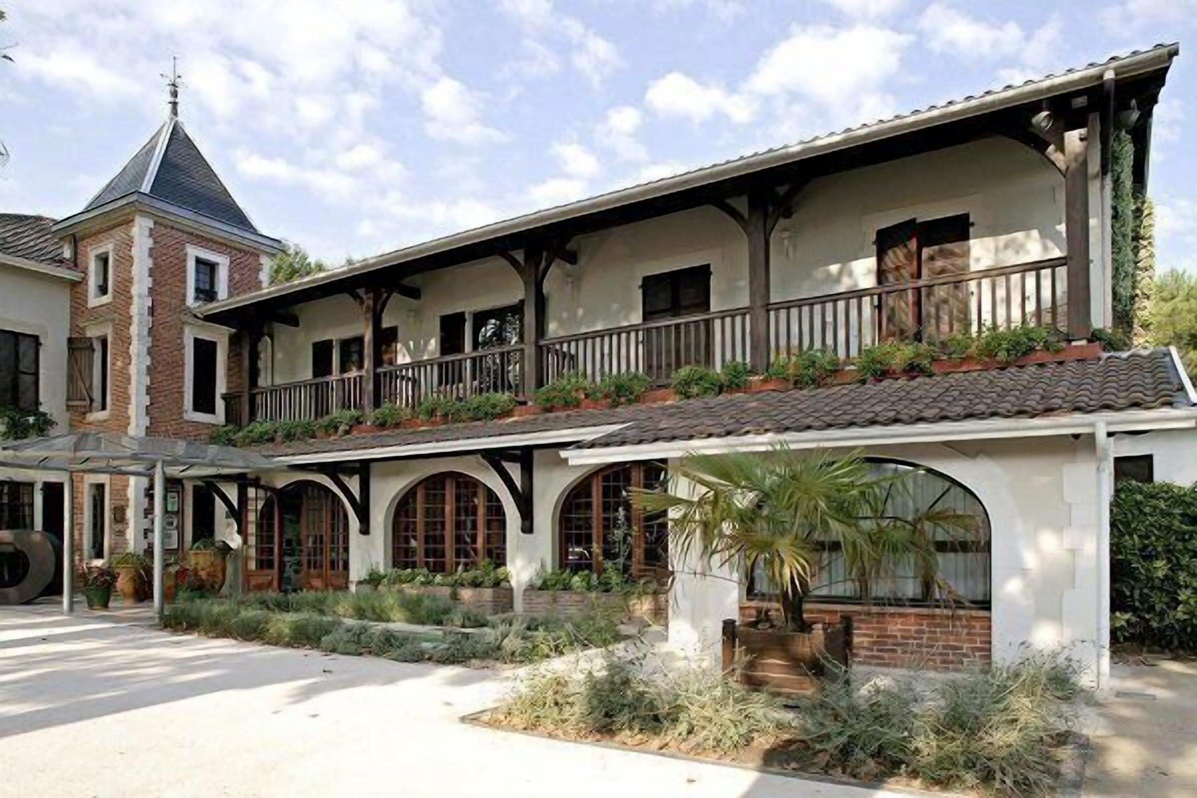 A two-story building with a balcony, arched windows, and a brick chimney.
