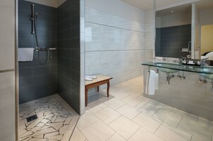 Un baño moderno con cabina de ducha de vidrio, un banco de madera y un lavamanos de vidrio con espejo.