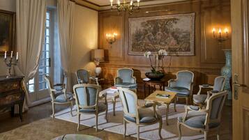 Un salón formal con una araña, un cuadro grande y varias sillas dispuestas alrededor de una mesa.