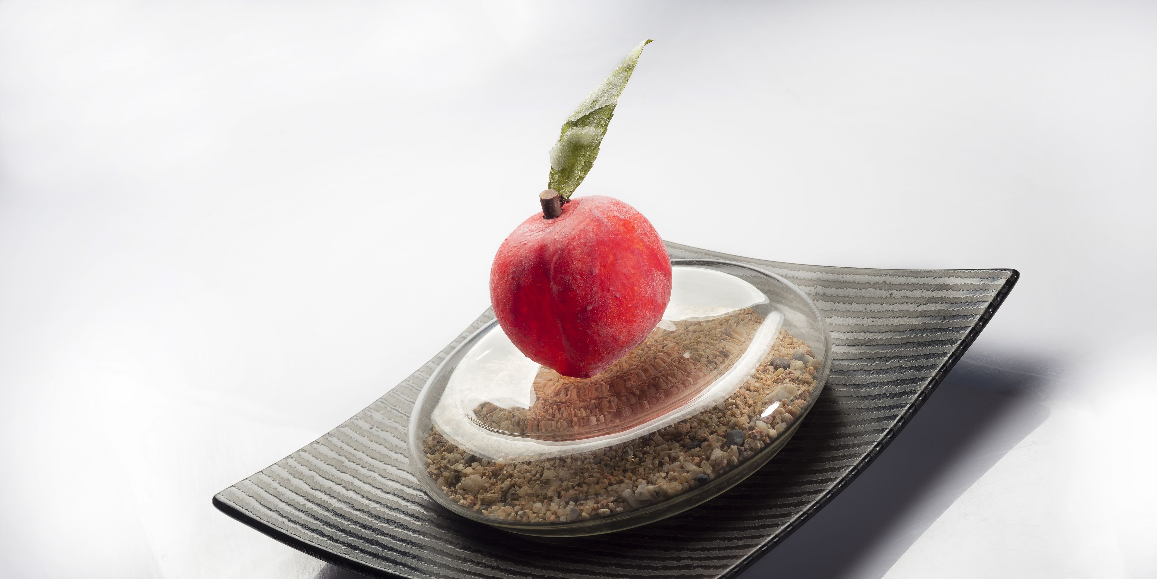 A clear glass bowl with a red fruit on top, placed on a textured surface.