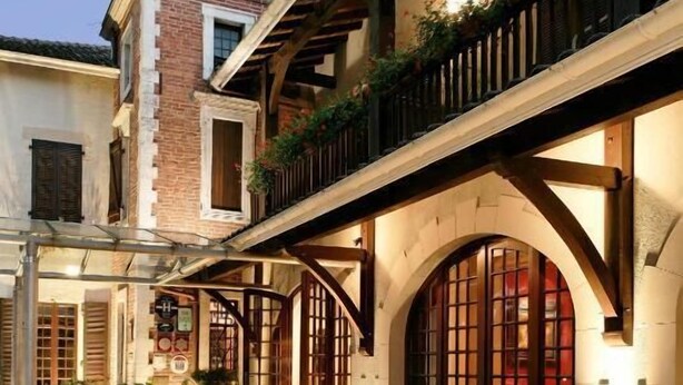A courtyard with a fountain, arched windows, and a brick building with a balcony. - LE RELAIS DE LA POSTE (Magescq)