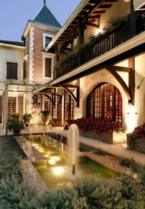 A courtyard with a fountain, arched windows, and a brick building with a balcony. - LE RELAIS DE LA POSTE (Magescq)