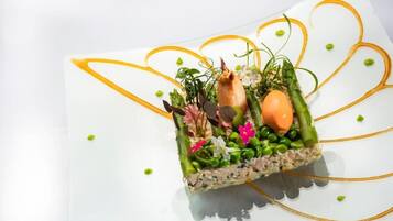Un plato cuadrado con una variedad de ingredientes y adornos, presentado sobre un plato blanco con un diseño de línea amarilla decorativa.
