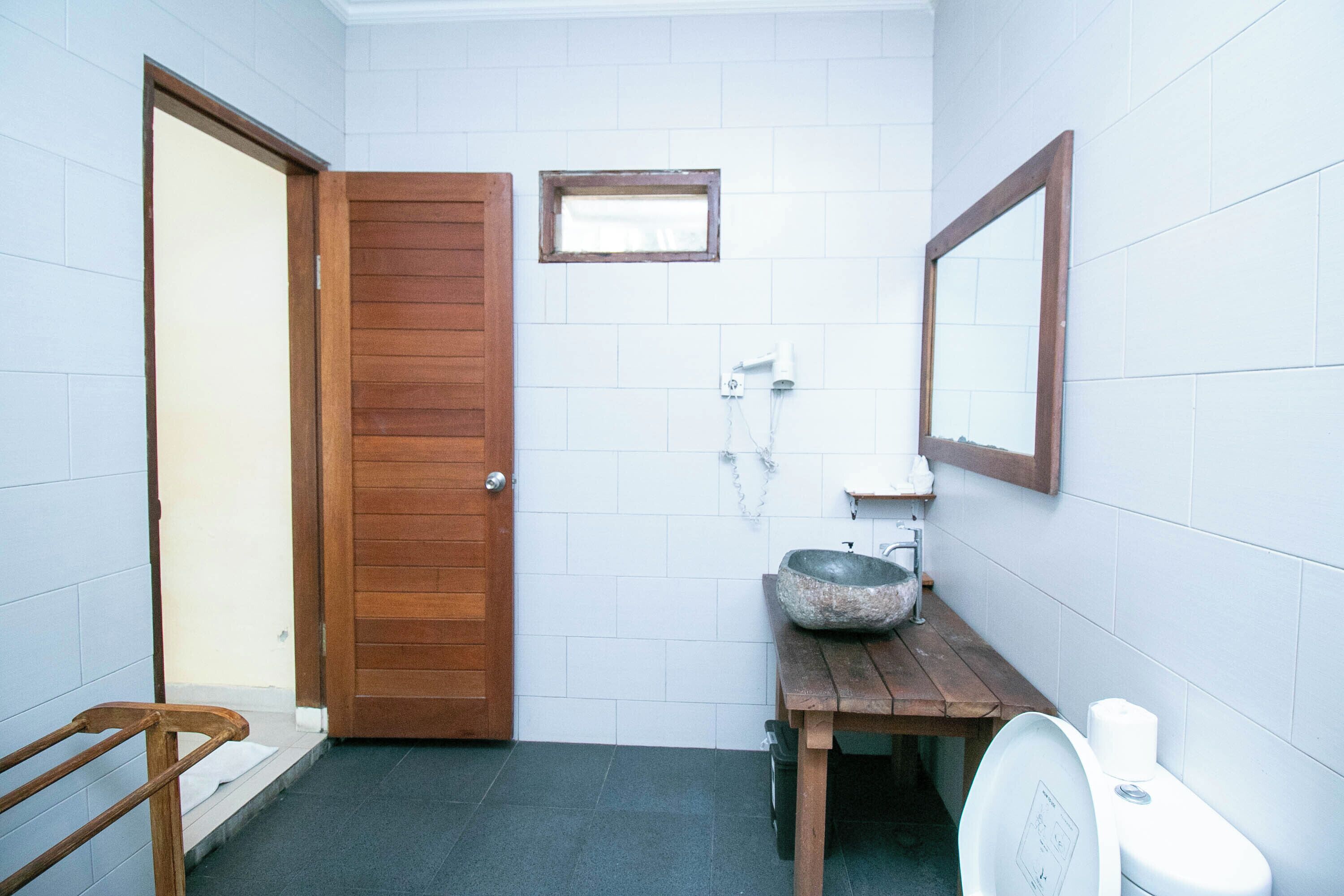 A bathroom with a wooden door, a small window, a sink with a stone basin, and a toilet.
