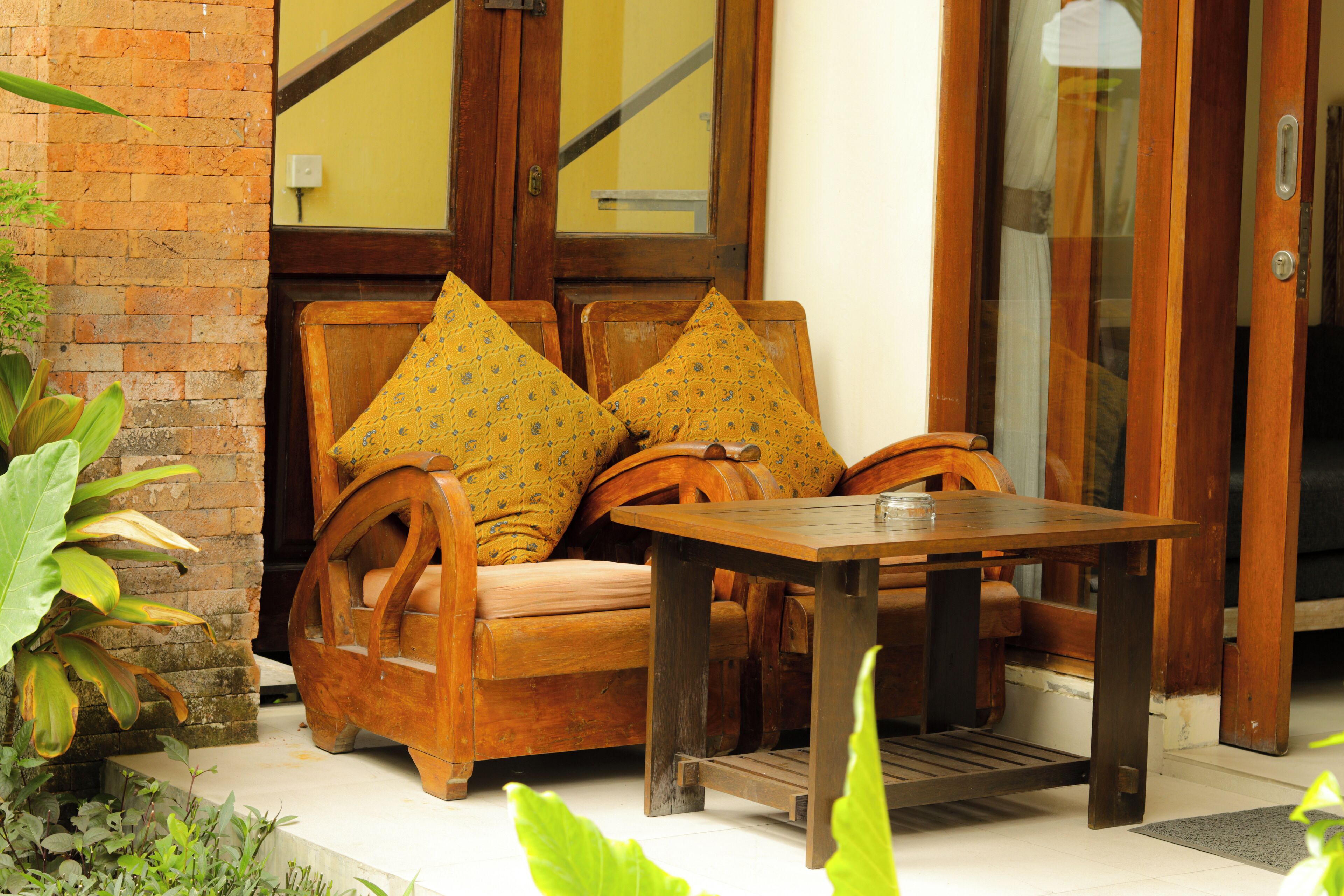 A wooden bench with cushions, a table, and a brick wall.