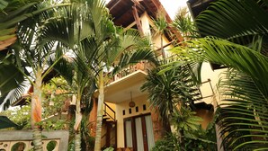 A two-story building with a balcony, surrounded by lush tropical plants. - Mina Pelasa Hotel and Resto (Legian)