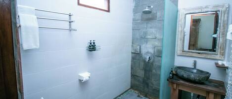 A bathroom with a toilet, a sink with a stone basin, a shower area, and a mirror above the sink.